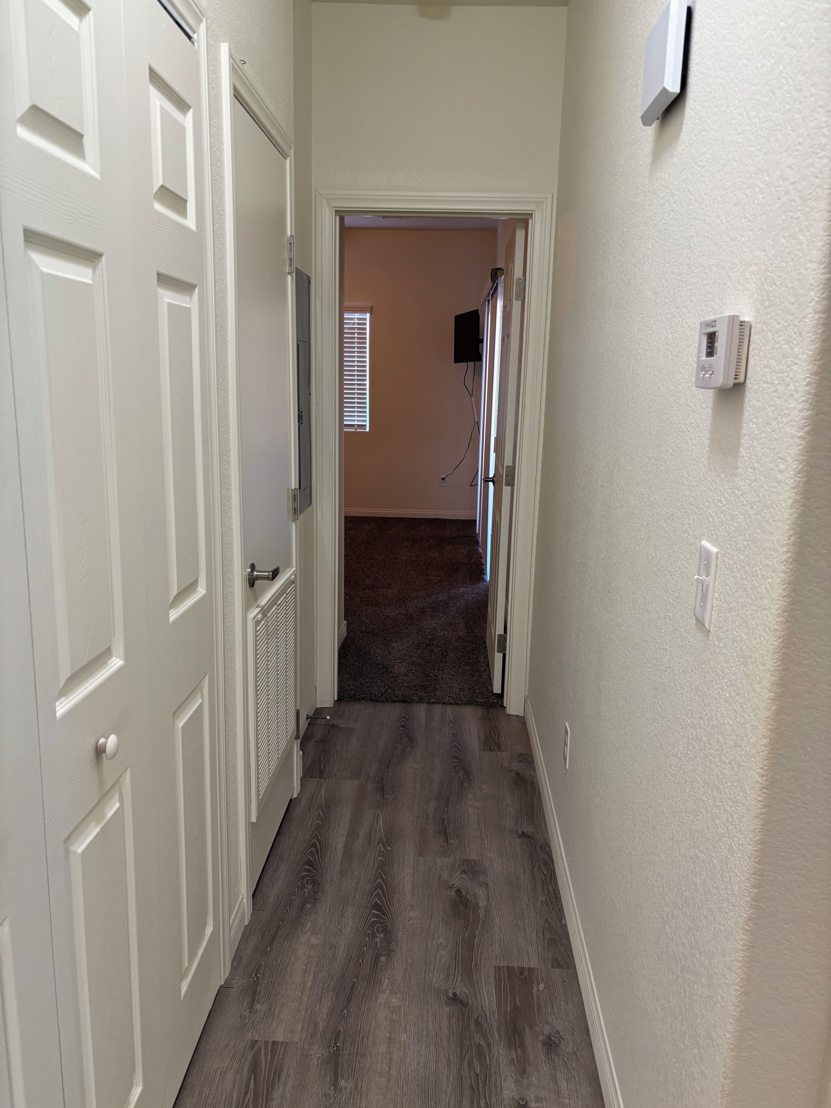 A hallway with a carpeted floor, white walls, and a door leading to another room.