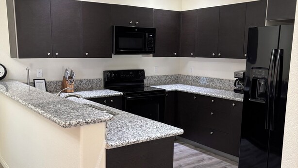 A modern kitchen with dark cabinetry, a granite countertop, a black stove, a microwave, and a refrigerator. - 3-bedroom condo in pleasant Mesquite with AC, WiFi. Enjoy your stay (Mesquite)