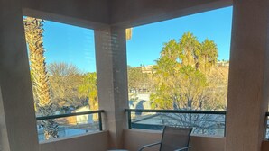 A balcony with a table and two chairs, offering a view of palm trees and buildings. - 3-bedroom condo in pleasant Mesquite with AC, WiFi. Enjoy your stay (Mesquite)
