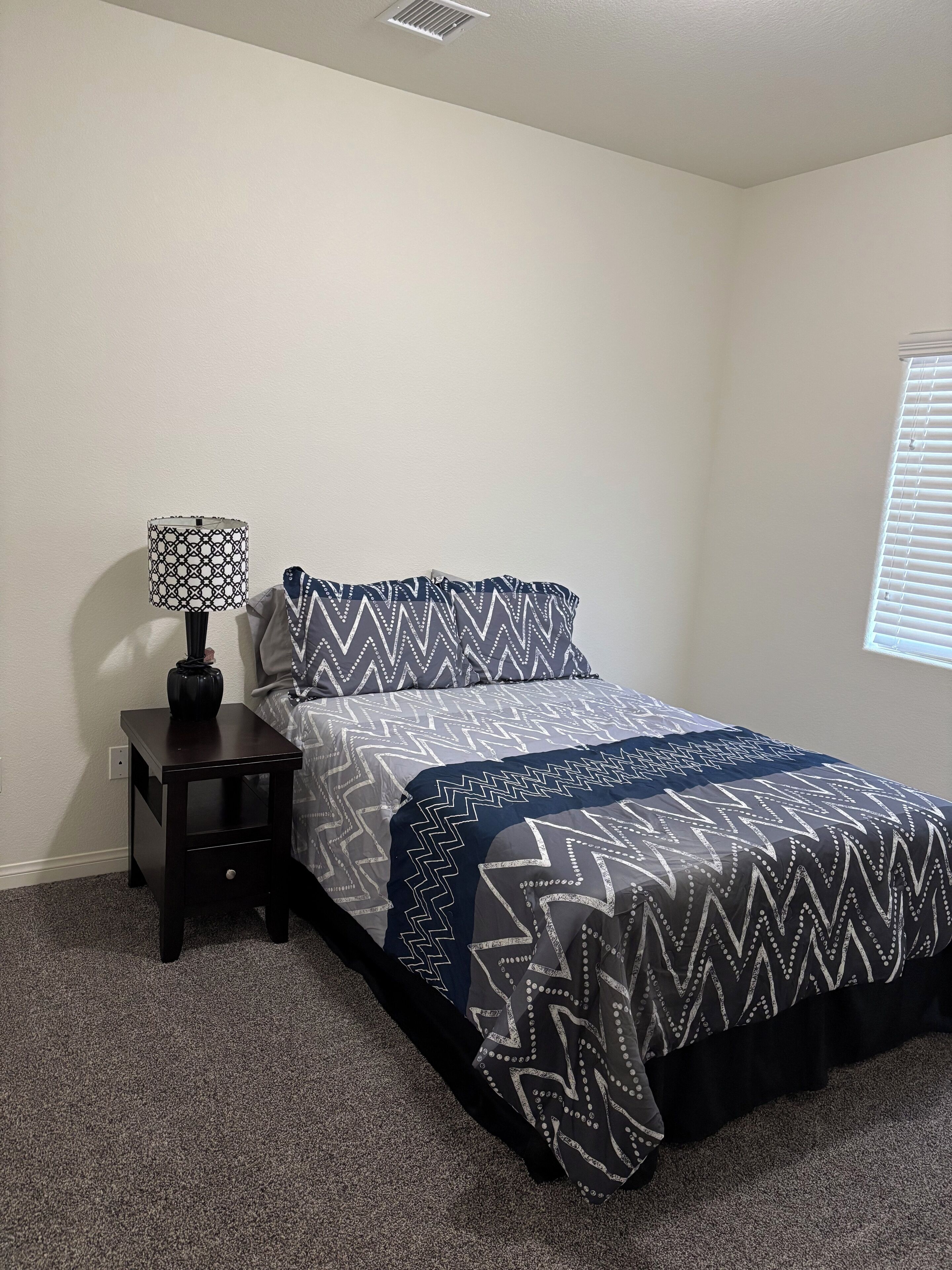A bedroom with a bed, a nightstand, a lamp, and a window.