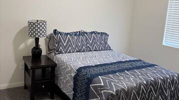 A bedroom with a bed, a nightstand, a lamp, and a window.