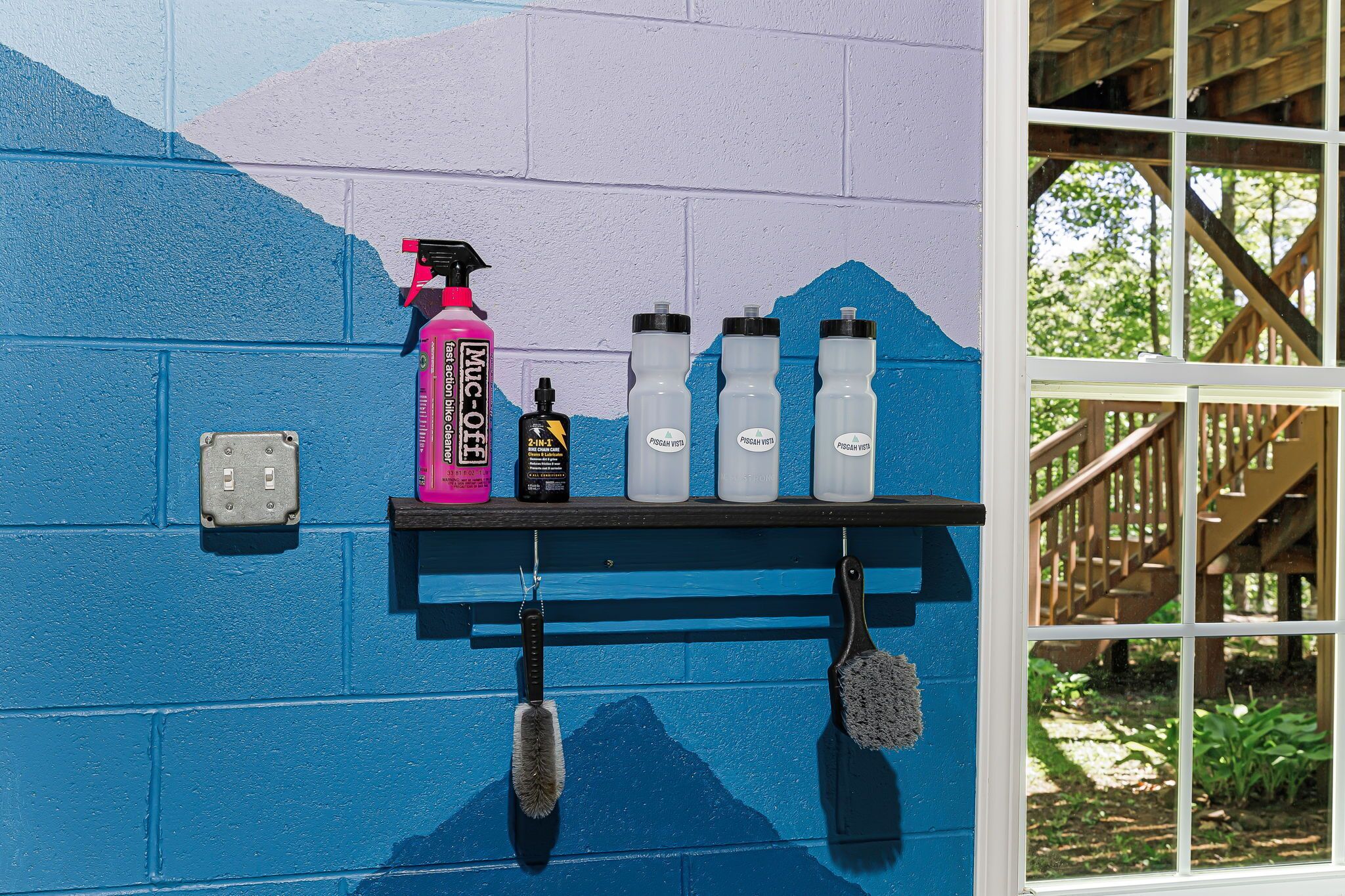 A wall-mounted shelf with cleaning supplies and a window with a view of a wooden deck and greenery.