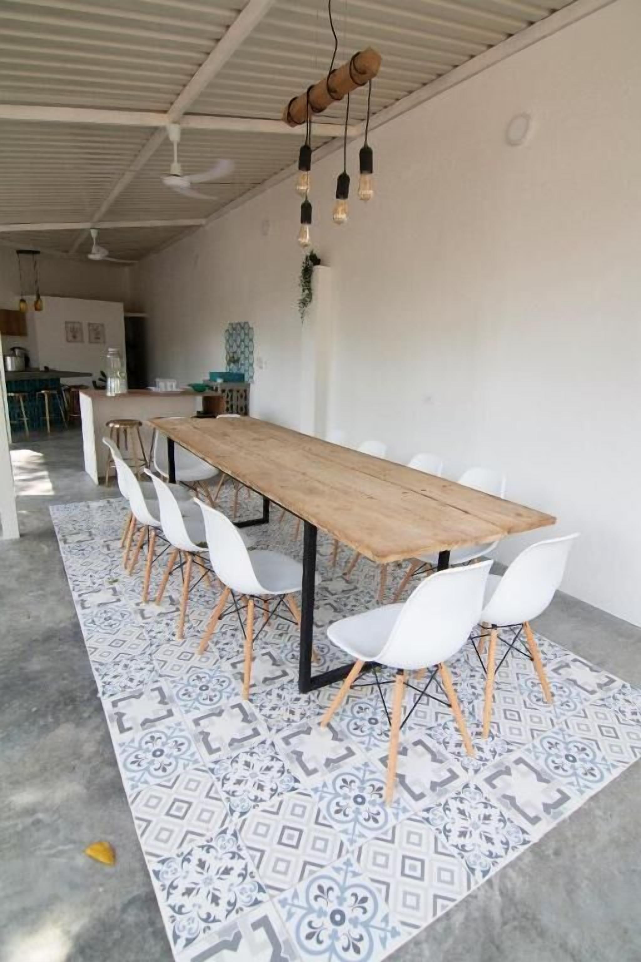 A spacious dining area with a long wooden table surrounded by white chairs, a patterned rug, and pendant lighting.