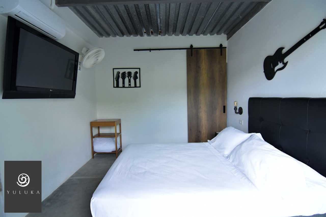 A bedroom with a bed, a TV, a guitar, and a wooden shelf.