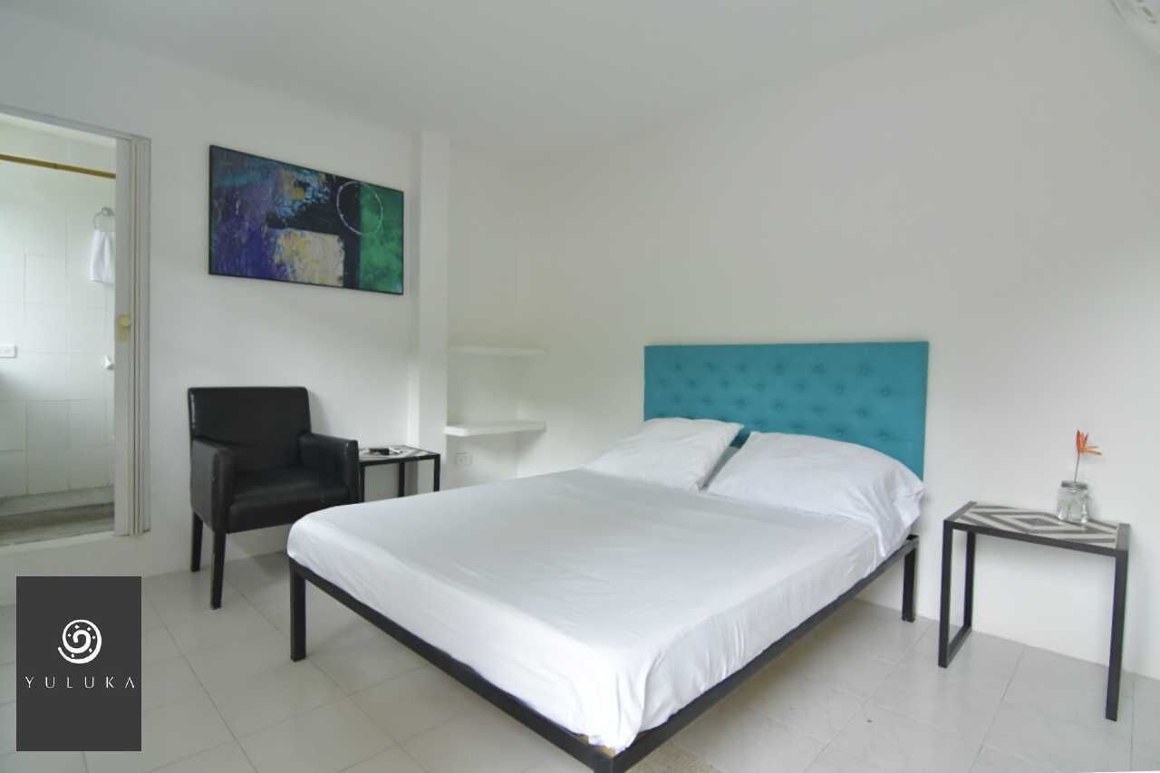 Una habitación de hotel moderna con una cama grande, una silla negra, una mesita y un cuadro en la pared.