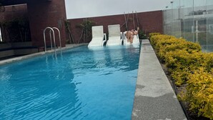 Una piscina con superficie de agua azul cristalina, rodeada por un suelo de hormigón y un muro de ladrillo.