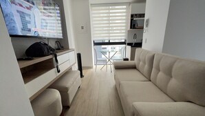 Una sala de estar moderna con un sofá color beige, un televisor de pantalla plana y una pequeña mesa de comedor.