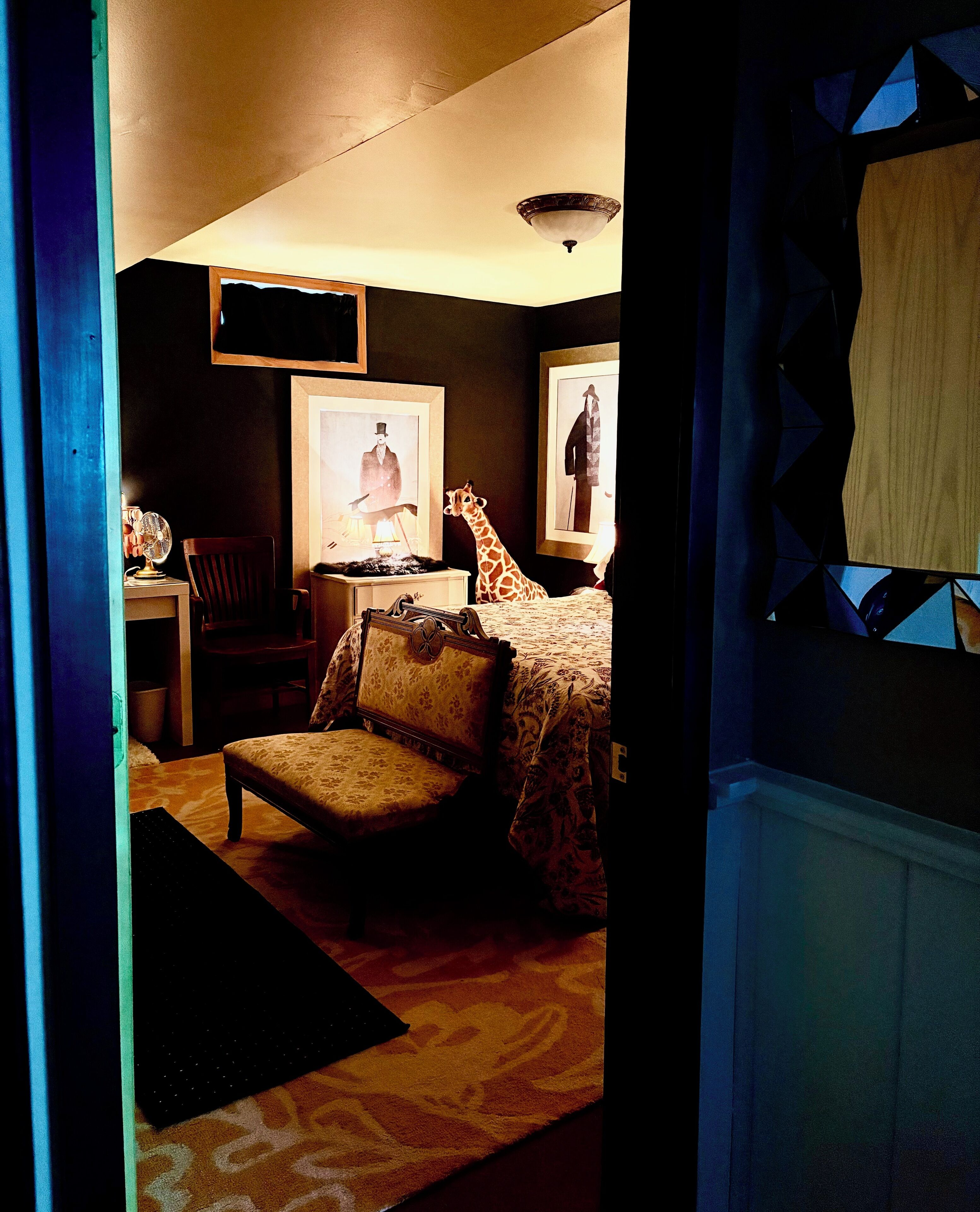 Un dormitorio con cama, una silla, un escritorio y dos cuadros en la pared.