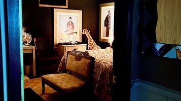 Un dormitorio con cama, una silla, un escritorio y dos cuadros en la pared.