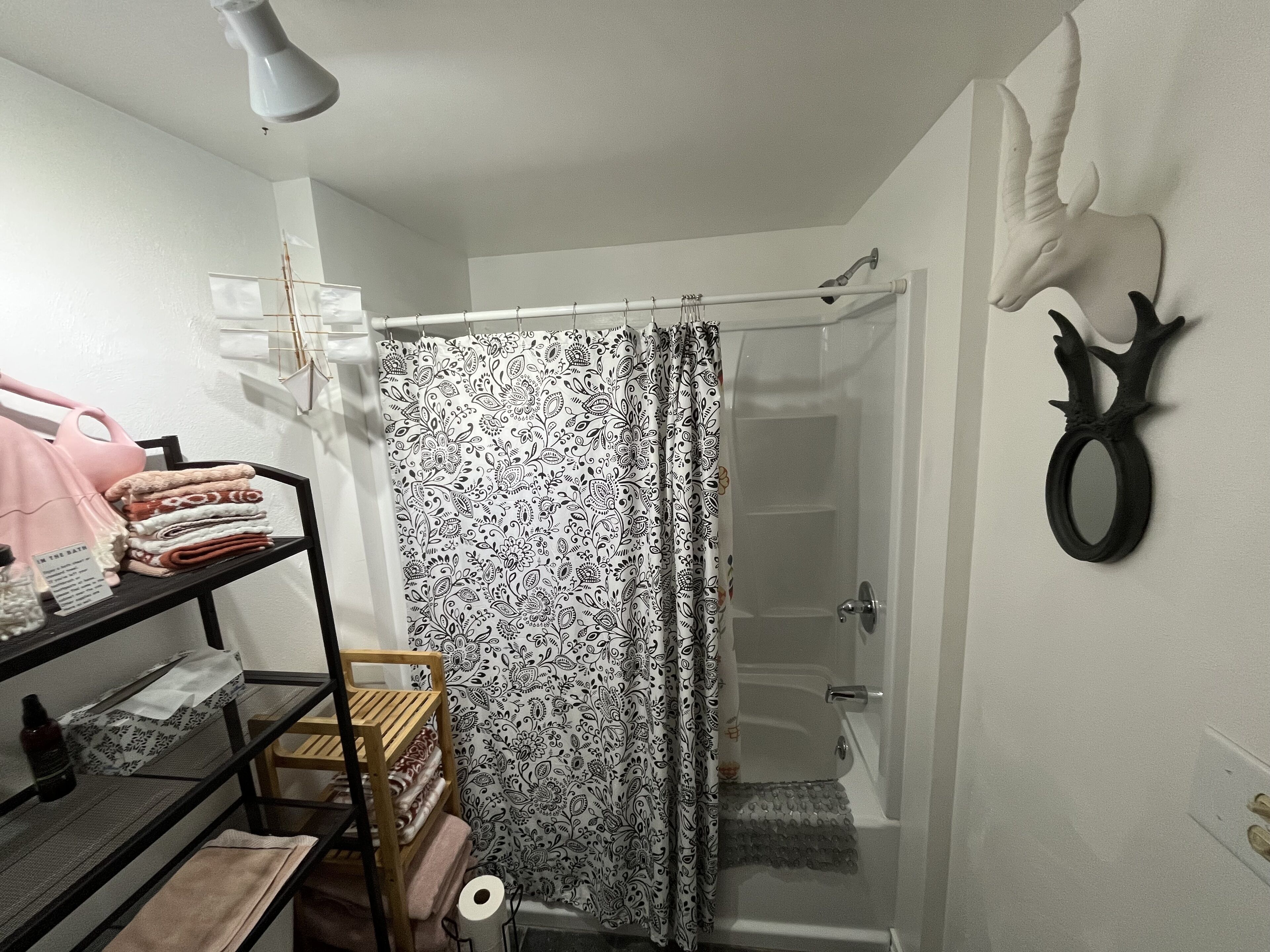 A bathroom with a shower curtain, a towel rack, a shelf with towels, and a wall-mounted mirror.