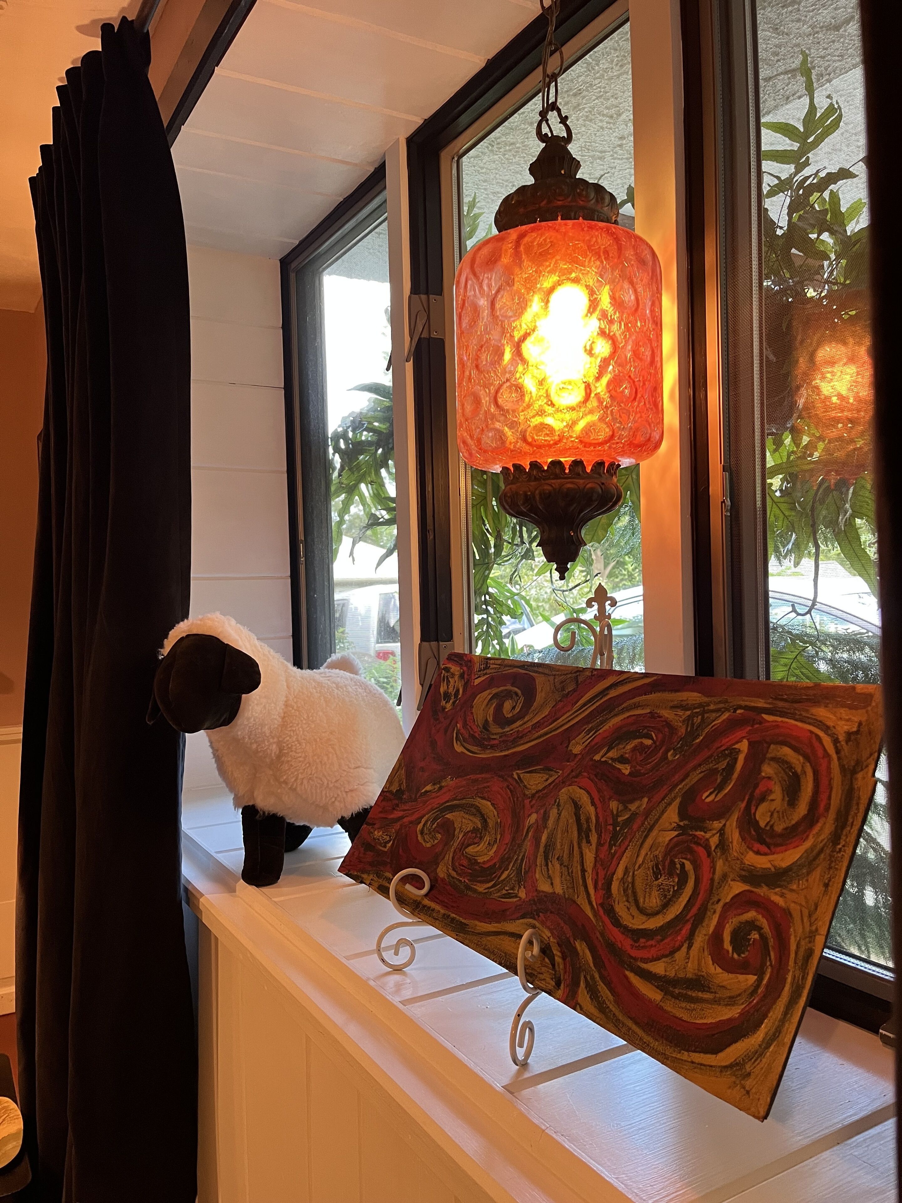 A window with a hanging lantern, a plush sheep, and a patterned cushion on a white ledge.