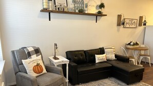 Un salón con un sillón gris, un sofá modular negro, una mesita blanca y una lámpara decorativa.
