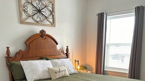 Una cama bien hecha con colcha verde, cabecera de madera y un adorno decorativo en la pared superior.