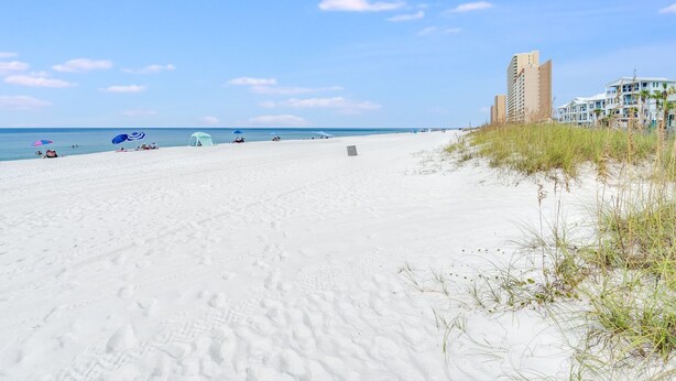 A beach with white sand, a few umbrellas, and a tall building in the background.