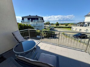 A balcony with a table and chairs, a view of a parking area, and a building in the background.
