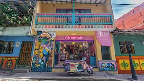 Un hotel colorido con una fachada vibrante, un balcón con barandillas azules y una moto estacionada afuera.