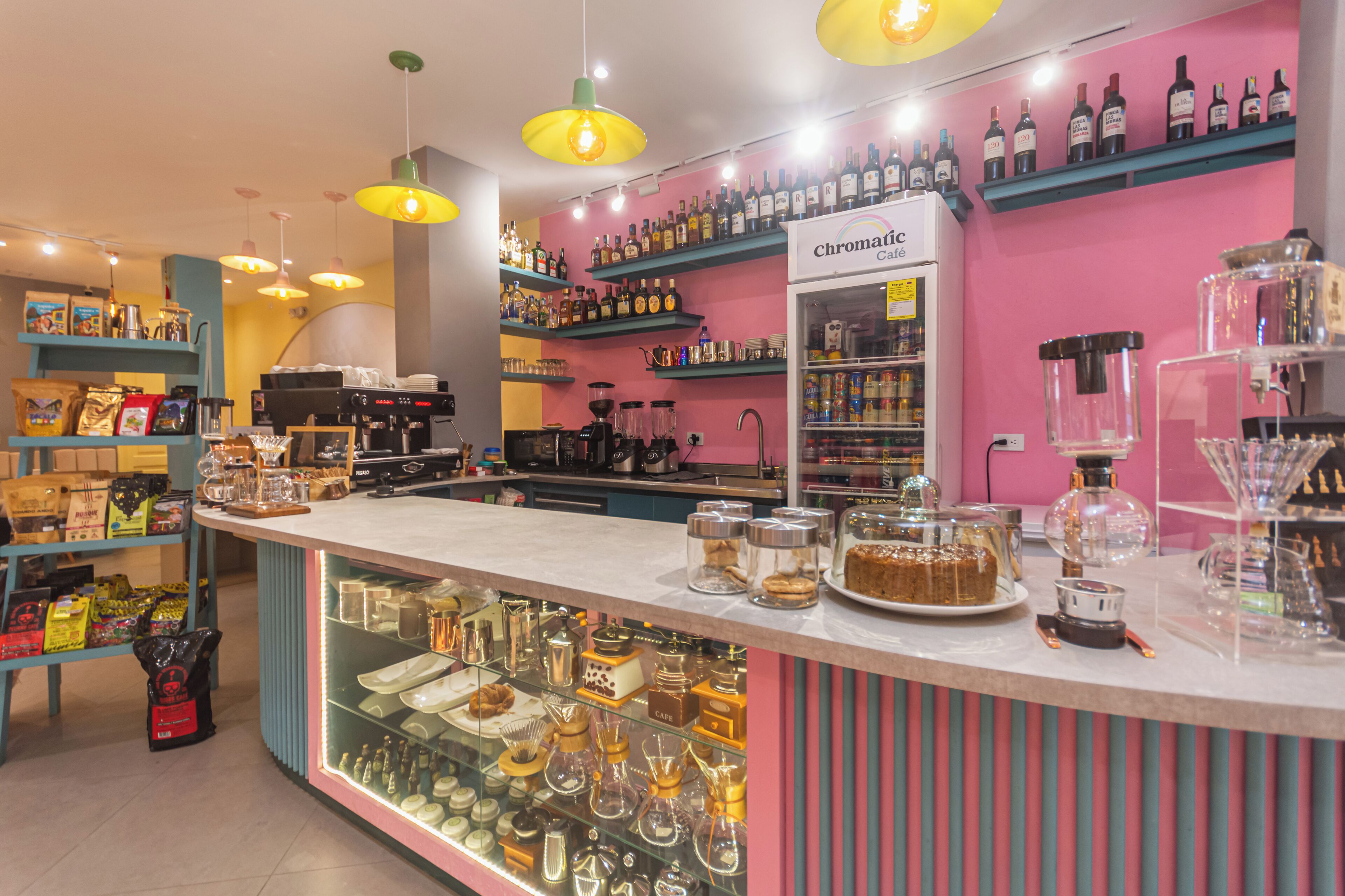 Un café amb un taulell que mostra pastissos i maquinària de cafè. Es veuen estanteries amb ampolles i una màquina de cafè al fons.