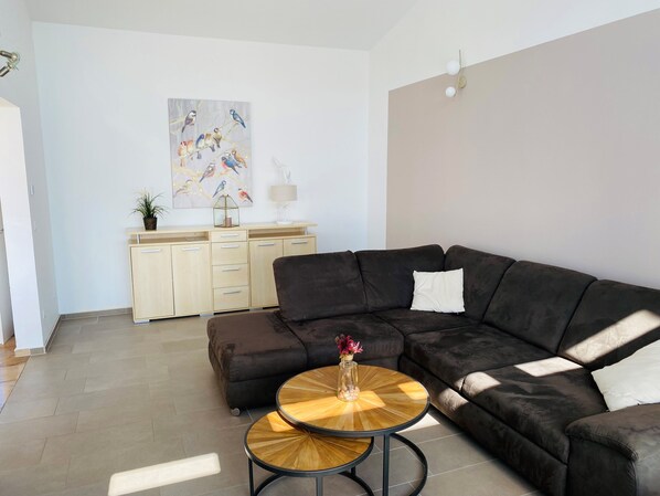 A modern living room with a dark brown sectional sofa, a wooden coffee table, a beige cabinet with drawers, a painting of birds on the wall, and a lamp.