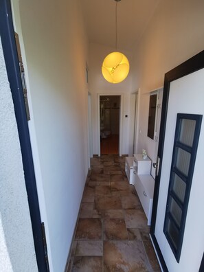 A hallway with a tiled floor, a white door with a black frame, and a hanging light fixture.