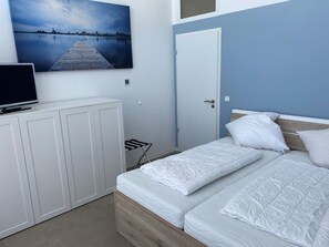 A bedroom with a bed, a TV on a cabinet, and a cityscape painting on the wall.