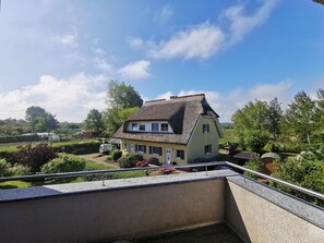 A traditional house with a thatched roof, surrounded by greenery and a clear sky.