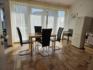 A dining area with a table, chairs, and a kitchen with a refrigerator and oven.