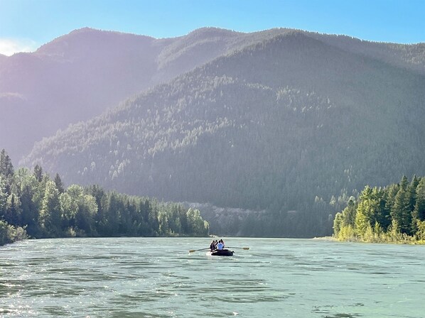 Un kayakista en un lago tranquilo con montañas boscosas al fondo.