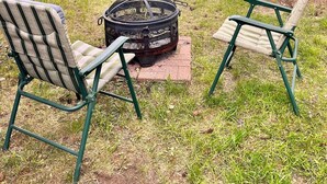 A backyard with a fire pit, two green lawn chairs, and a wooden fence.