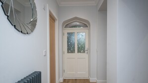 A hallway with a white door, a radiator, and a wall-mounted mirror. - Historical Holmehill Lodge - a family friendly home for get togethers! (Dunblane)