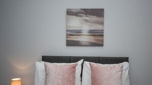A neatly made bed with two pillows, a bedside lamp, and a wall-mounted artwork of a beach scene. - Historical Holmehill Lodge - a family friendly home for get togethers! (Dunblane)