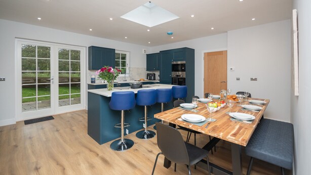 A modern kitchen with a central island, bar stools, and a dining table set for six. - Historical Holmehill Lodge - a family friendly home for get togethers! (Dunblane)