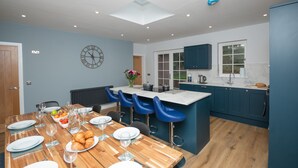 A modern kitchen with a central island, bar stools, and a dining table set for a meal. - Historical Holmehill Lodge - a family friendly home for get togethers! (Dunblane)