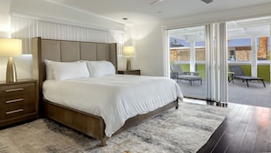 Ett modernt hotellrum med en stor säng, två sängbord med lampor, en takfläkt och utsikt över den utomhusbelägna uteplatsen.