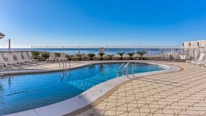 Ein Pool mit freiem Blick auf das Meer, umgeben von Liegestühlen und einer gefliesten Terrasse.