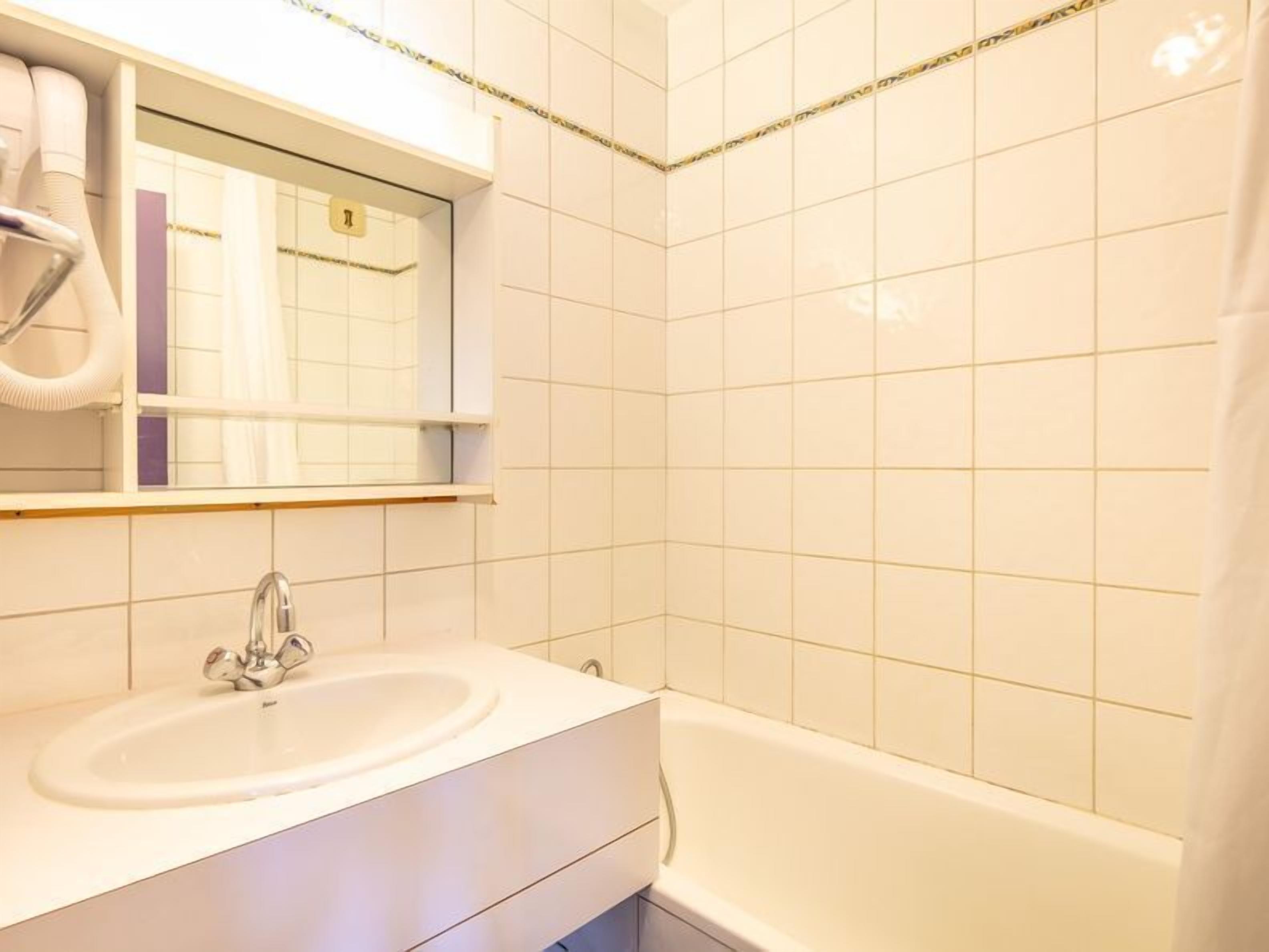 Une salle de bain avec un lavabo blanc, un miroir et une baignoire.