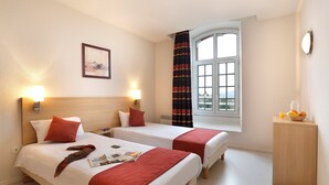 Une chambre d’hôtel avec deux lits, une fenêtre avec des rideaux, une table de chevet avec un panier de fruits et un tableau accroché au mur.