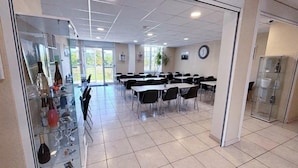 Une salle de conférence avec des tables et des chaises, une vitrine contenant des bouteilles et une horloge au mur.