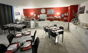 Una zona de menjador amb taules preparades per a les refeccions, una cuina al fons i un rellotge a la paret.