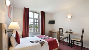A hotel room with a bed, a desk, a chair, a TV, and a window with curtains. - Value Studio: Cozy, Kitchenette, Free Wi-Fi (Epernay)