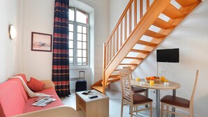 A modern room with a sofa, a small table with chairs, a staircase, and a window with curtains. - Cozy Apt w/ Kitchen + Free Wi-Fi! On-Site Parking (Epernay)