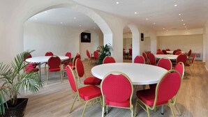 Une salle de conférence avec des tables rondes et des chaises rouges, des murs blancs et un plancher en bois.