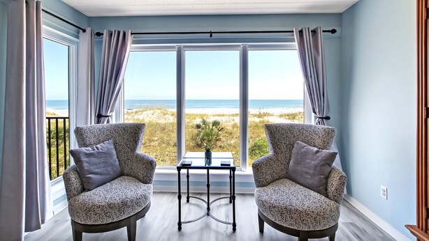 Una habitación con dos sillones estampados, una mesita y vista a la playa a través de amplios ventanales.