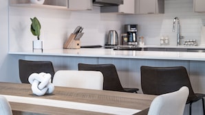 Une cuisine moderne avec un plan de travail blanc, une machine à café et un four à micro-ondes. On y trouve une plante sur le plan de travail et un bloc à couteaux.