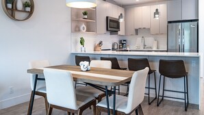 Une cuisine moderne dotée d’un îlot central, de meubles blancs, d’appareils électroménagers en acier inoxydable et de luminaires suspendus.