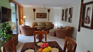 A living room with a sofa, two armchairs, a coffee table, and a dining table set with plates, glasses, and fruit. - 2br White Sands Village condo right at the beach (Kailua Kona)