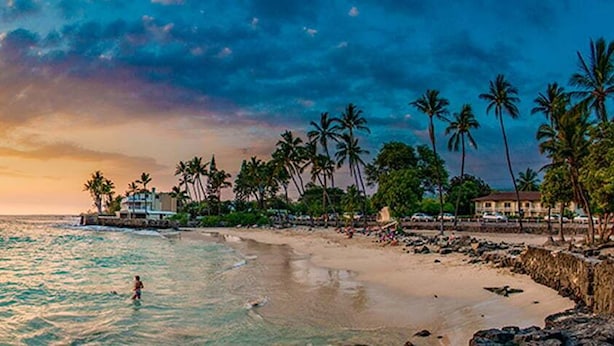 A beach with a sunset, palm trees, and a building near the water. - 2br White Sands Village condo right at the beach (Kailua Kona)