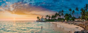 A beach with a sunset, palm trees, and a building near the water. - 2br White Sands Village condo right at the beach (Kailua Kona)