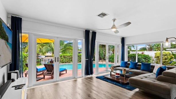A spacious living room with a large sofa, a TV, and a pool view through glass doors. - Fort Lauderdale~River Access~Kayaks~Heated Pool (Fort Lauderdale)