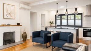 A modern living room with a fireplace, two blue armchairs, a brown leather sofa, and a kitchen in the background. - Modern family home in a leafy riverside suburb  (Graceville)