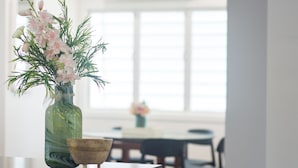 A vase with flowers on a table in a room with a window and a dining area in the background. - Modern family home in a leafy riverside suburb  (Graceville)